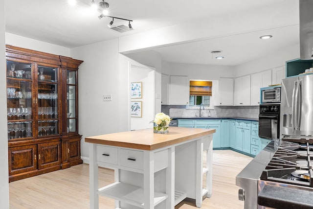 kitchen with black oven, butcher block countertops, light wood-type flooring, stainless steel refrigerator with ice dispenser, and visible vents