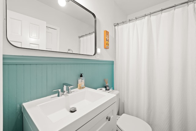 bathroom featuring vanity, toilet, curtained shower, and a wainscoted wall