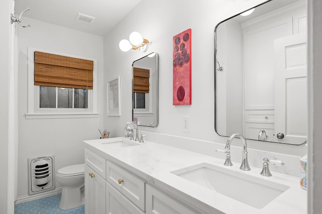 bathroom with a sink, heating unit, toilet, and double vanity