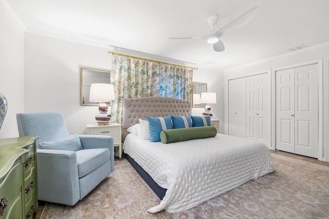 bedroom with crown molding, visible vents, two closets, wood finished floors, and ceiling fan