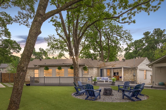 back of house at dusk with an outdoor living space with a fire pit, a patio, a yard, and stone siding