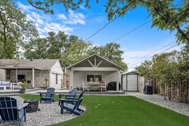 rear view of house featuring an outdoor structure, an outdoor living space with a fire pit, fence, a shed, and a yard
