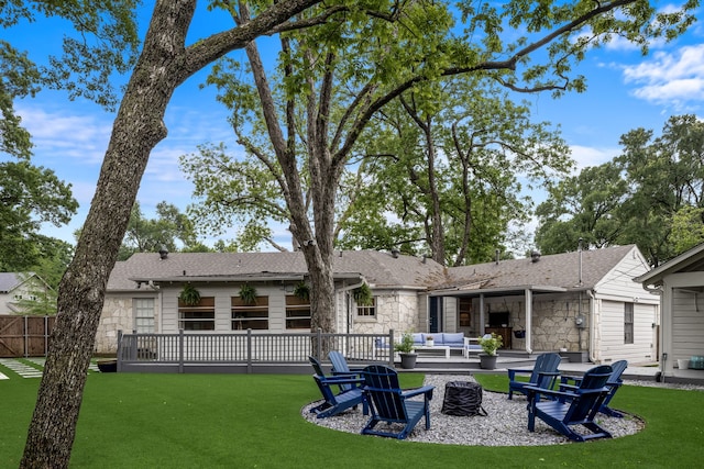 rear view of house featuring roof with shingles, stone siding, an outdoor living space with a fire pit, a patio, and a yard