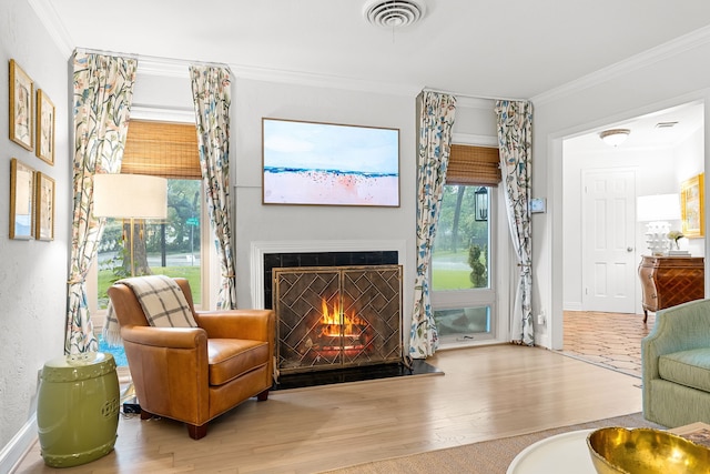 living area featuring a warm lit fireplace, baseboards, wood finished floors, visible vents, and ornamental molding