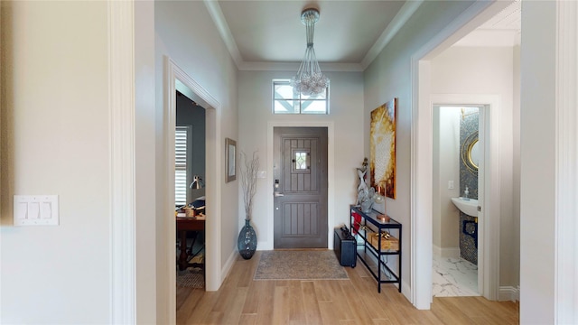 foyer with an inviting chandelier, ornamental molding, baseboards, and light wood-style flooring