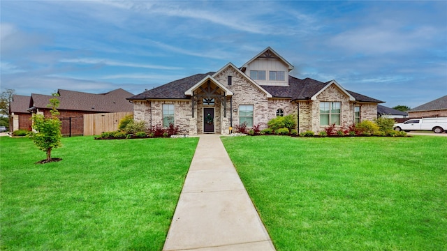 view of front of home featuring brick siding, fence, roof with shingles, and a front lawn