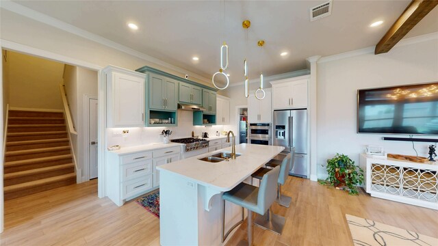 kitchen featuring light wood-style floors, a center island with sink, under cabinet range hood, a sink, and stainless steel appliances