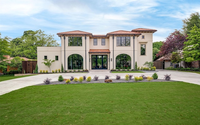 mediterranean / spanish-style home featuring curved driveway, a front lawn, and a tiled roof