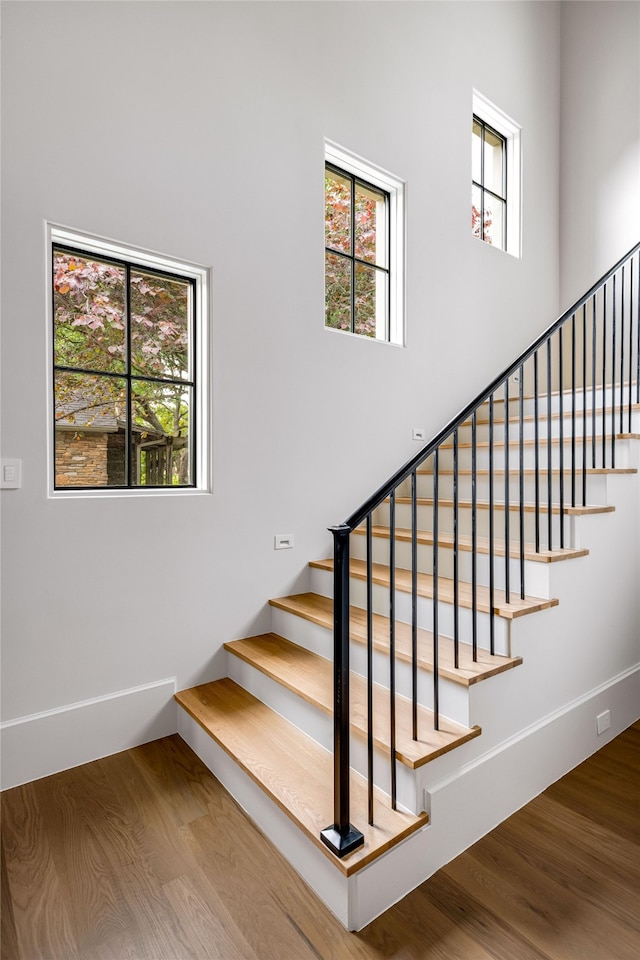 stairs with baseboards, a towering ceiling, and wood finished floors