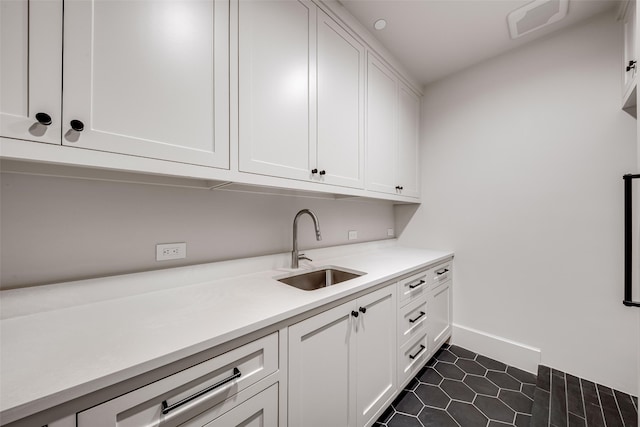 washroom featuring baseboards, a sink, visible vents, and dark tile patterned flooring