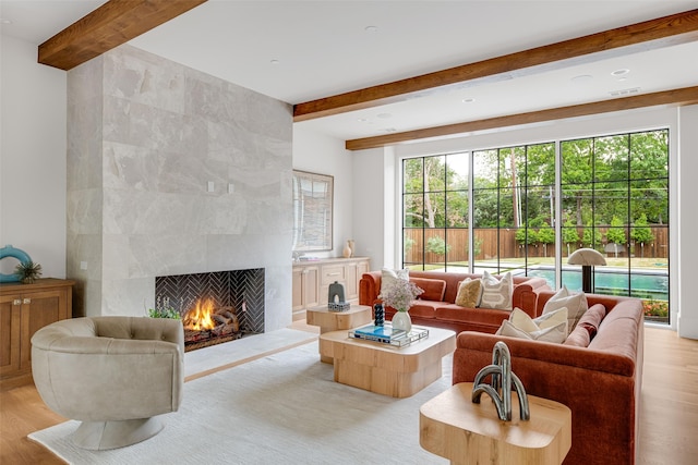 living room with light wood-type flooring, a tile fireplace, and beamed ceiling
