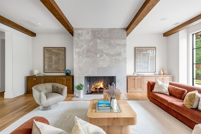 living room with visible vents, a large fireplace, beam ceiling, and light wood-style floors