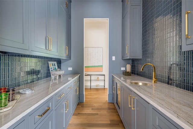 kitchen with a sink, decorative backsplash, light stone countertops, and light wood-style flooring