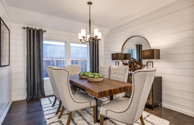 dining room with an inviting chandelier, wood walls, wood-type flooring, lofted ceiling, and baseboards