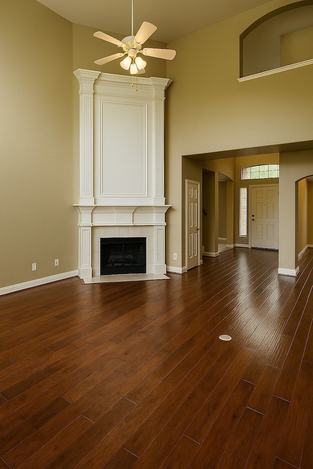 4605 Stargazer Dr, Plano, TX 75024 - unfurnished living room featuring a ceiling fan, dark wood-style flooring, a towering ceiling, a tiled fireplace, and baseboards