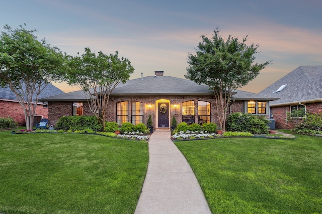 ranch-style home with brick siding, a shingled roof, a front lawn, and a chimney