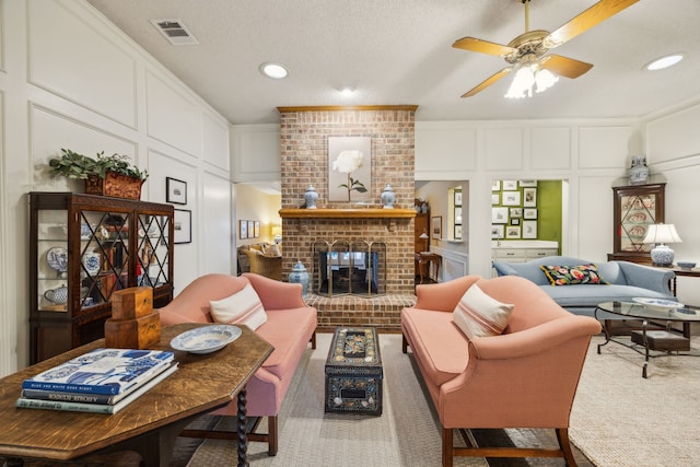 carpeted living area featuring ceiling fan, visible vents, a fireplace, a decorative wall, and recessed lighting