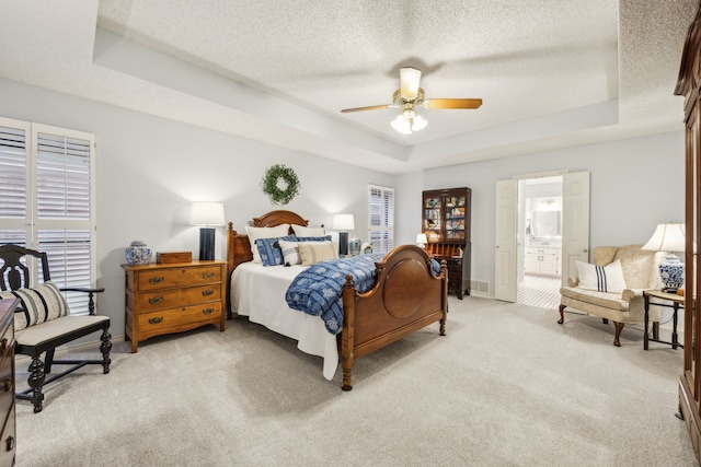 bedroom with ceiling fan, a textured ceiling, baseboards, light carpet, and a tray ceiling