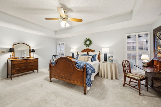 carpeted bedroom featuring baseboards, ceiling fan, a tray ceiling, and a textured ceiling