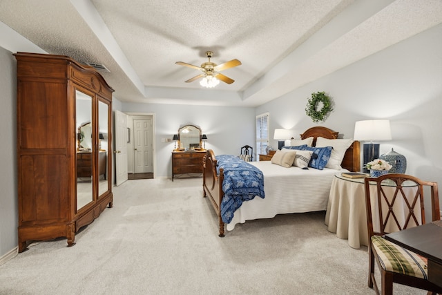 bedroom featuring a ceiling fan, a textured ceiling, visible vents, light colored carpet, and a raised ceiling