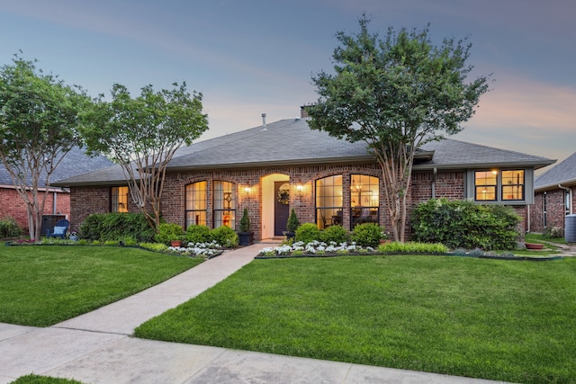 single story home featuring brick siding, cooling unit, roof with shingles, and a front lawn