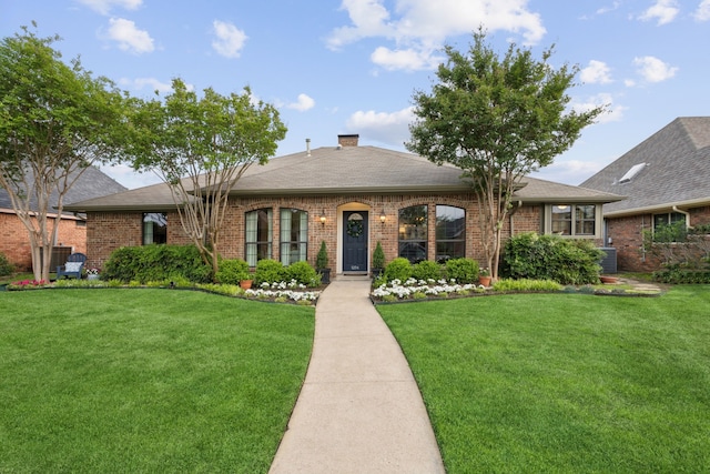 single story home featuring roof with shingles, a chimney, a front yard, and brick siding