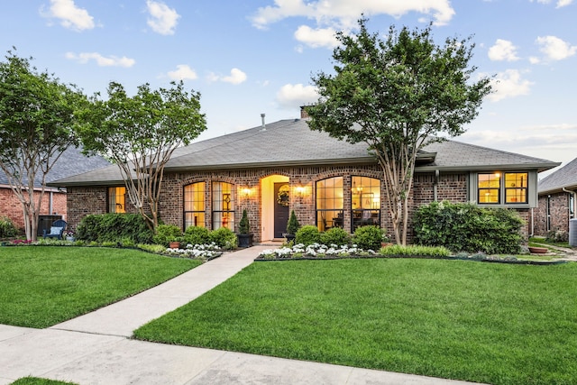 ranch-style home featuring a shingled roof, a front lawn, and brick siding