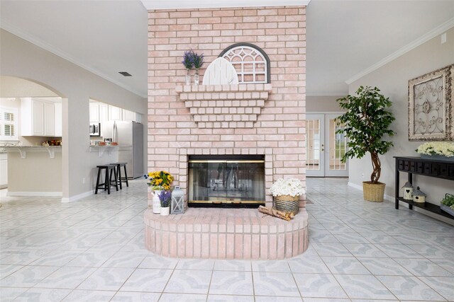 living area featuring visible vents, ornamental molding, a brick fireplace, arched walkways, and light tile patterned floors