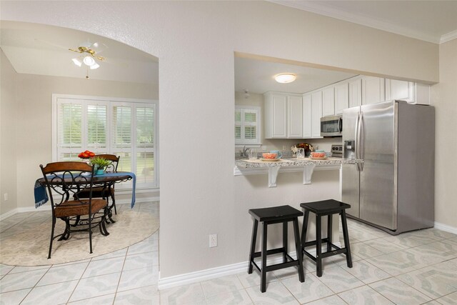 kitchen featuring light countertops, white cabinets, a breakfast bar, stainless steel appliances, and light tile patterned flooring