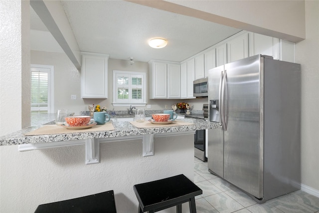 kitchen with a peninsula, a kitchen bar, light countertops, white cabinetry, and stainless steel appliances