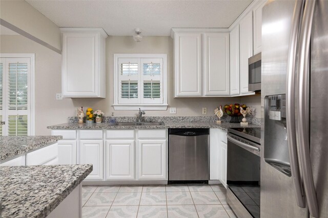 kitchen with light stone countertops, a sink, stainless steel appliances, white cabinetry, and light tile patterned floors