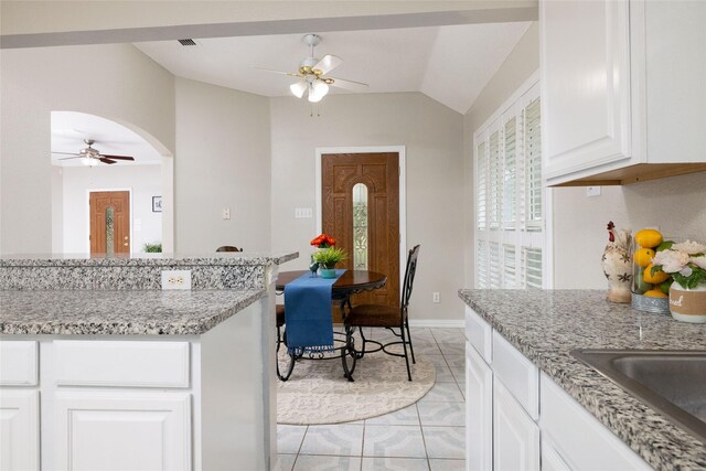 kitchen featuring ceiling fan, light stone counters, arched walkways, white cabinetry, and vaulted ceiling