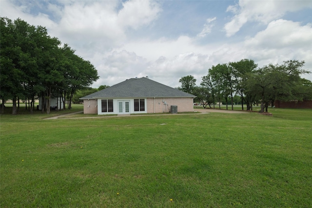 rear view of property featuring a lawn, roof with shingles, central AC, and french doors