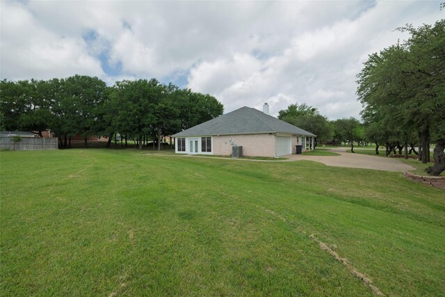 view of yard with a garage, fence, driveway, and cooling unit
