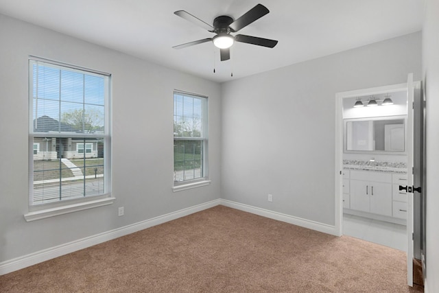 unfurnished bedroom featuring light carpet, baseboards, ceiling fan, connected bathroom, and a sink