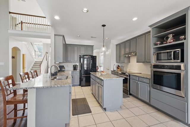 kitchen featuring stainless steel appliances, gray cabinets, decorative backsplash, and a sink