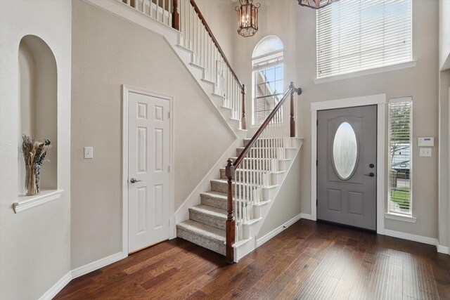 foyer with stairs, a towering ceiling, a notable chandelier, and hardwood / wood-style flooring