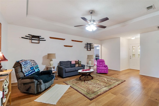living area with a ceiling fan, visible vents, light wood finished floors, and a raised ceiling