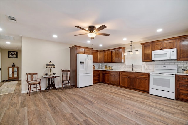 kitchen featuring visible vents, white appliances, a sink, light wood-style flooring, and backsplash