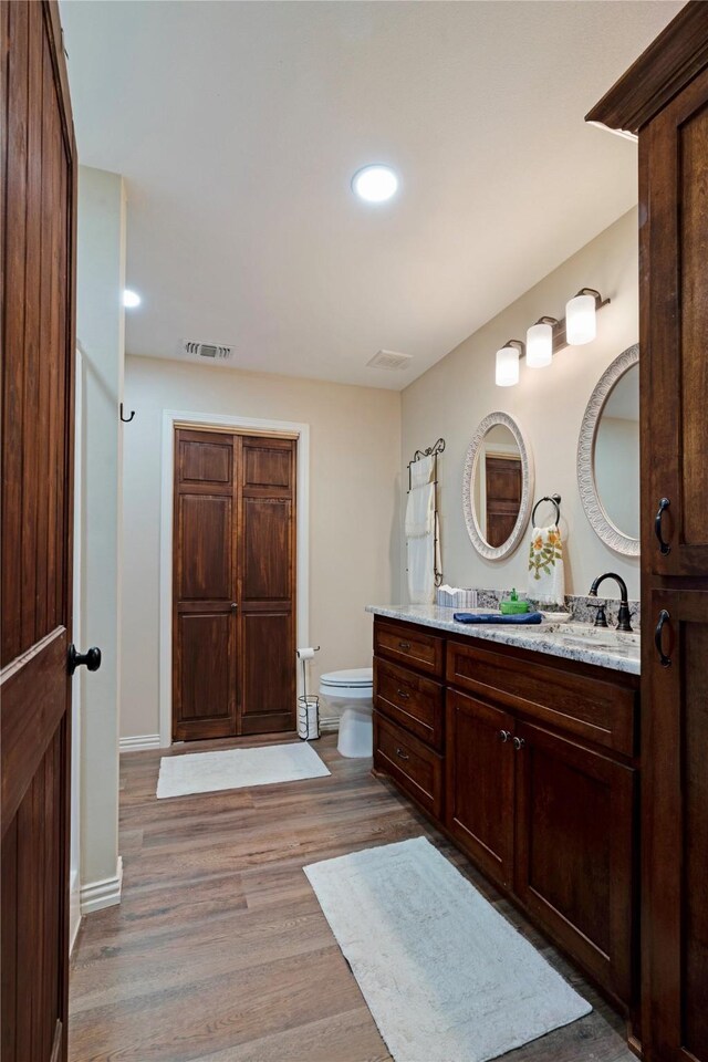 bathroom featuring double vanity, visible vents, wood finished floors, toilet, and recessed lighting