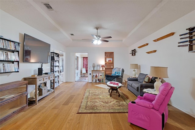 living room with a raised ceiling, ceiling fan, light wood finished floors, and visible vents