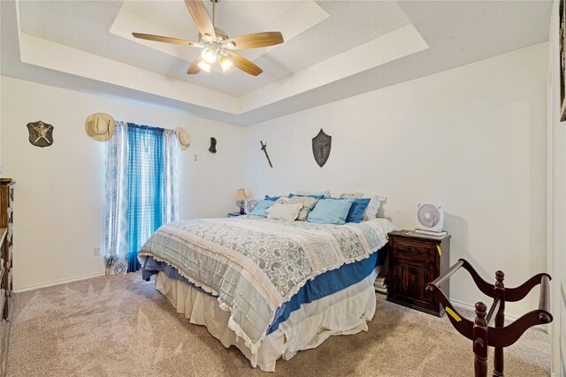 bedroom with baseboards, a tray ceiling, light carpet, and ceiling fan