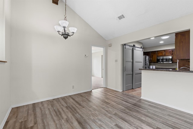 interior space featuring a chandelier, light wood-type flooring, a barn door, and visible vents