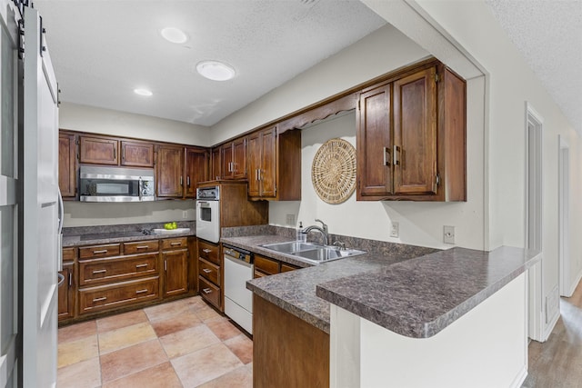 kitchen featuring a peninsula, dark countertops, white appliances, a textured ceiling, and a sink