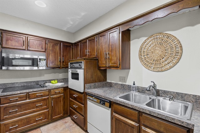 kitchen featuring a textured ceiling, dark countertops, a sink, light tile patterned floors, and white appliances