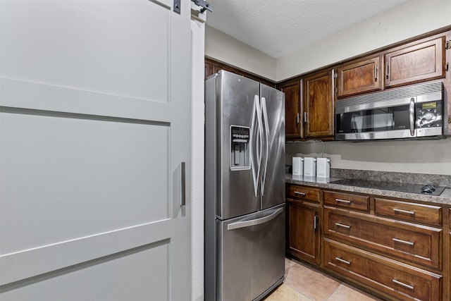 kitchen featuring a textured ceiling, dark stone countertops, appliances with stainless steel finishes, and light tile patterned floors