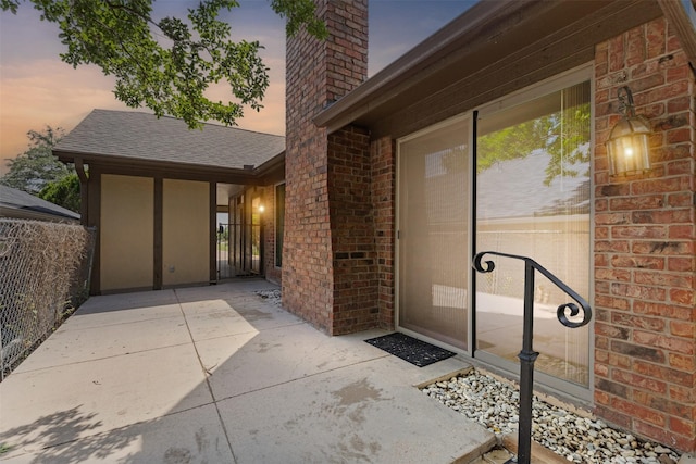 doorway to property featuring brick siding, roof with shingles, fence, and a chimney