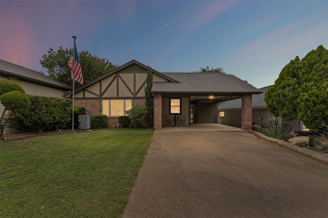 english style home with roof with shingles, a front lawn, brick siding, an attached carport, and driveway