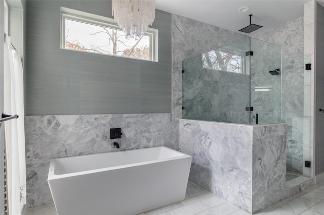 bathroom with a notable chandelier, tile walls, a freestanding bath, and a stall shower