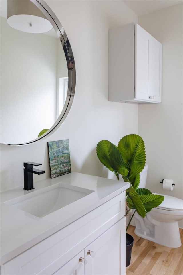 half bathroom featuring toilet, wood finished floors, and vanity